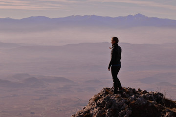 GIRL LOOKING AT A GREAT VALLEY FROM THE SUMMIT OF A MOUNTAIN