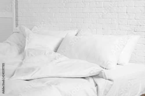 Fotomural Large comfortable bed with pillows and blanket near white brick wall indoors