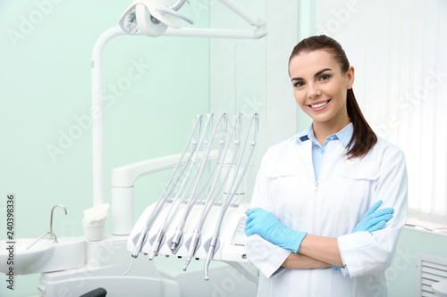 Fototapeta na szkło Young female dentist in white coat at workplace. Space for text