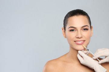 Poster - Young woman getting lips injection on grey background, space for text. Cosmetic surgery