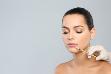 Poster - Young woman getting lips injection on grey background, space for text. Cosmetic surgery