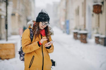 Cheerful gorgeous brunette in winter fashion holding smartphone on urban background