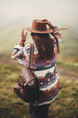 Sticker - Stylish hipster girl in hat walking on top of mountains. Happy young woman with backpack exploring misty mountains. Travel and wanderlust concept. Amazing atmospheric moment