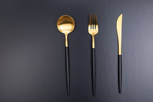 Set Of Black And Gold Cutlery On Black Background