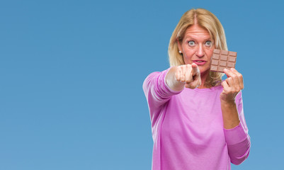 Canvas Print - Middle age blonde woman eating chocolate bar over isolated background pointing with finger to the camera and to you, hand sign, positive and confident gesture from the front