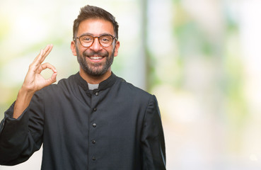 Wall Mural - Adult hispanic catholic priest man over isolated background smiling positive doing ok sign with hand and fingers. Successful expression.