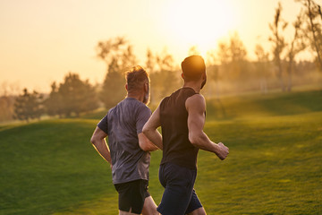 The two sportsmen running in the picturesque park on the sunset background