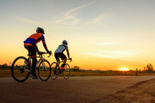 Men Ride Bicycles On The Road With Beautiful Colorful Sunset Sky. Sport And Active Life Concept.