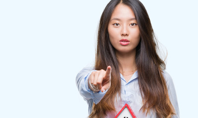 Sticker - Young asian woman real state agent holding house isolated background pointing with finger to the camera and to you, hand sign, positive and confident gesture from the front