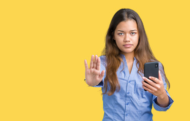 Canvas Print - Young beautiful brunette business woman using smartphone over isolated background with open hand doing stop sign with serious and confident expression, defense gesture