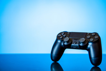 Wall Mural - modern black gamepad on a glossy surface and a glowing blue