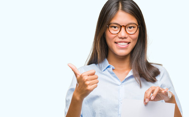 Sticker - Young asian woman over isolated background holding blank paper happy with big smile doing ok sign, thumb up with fingers, excellent sign