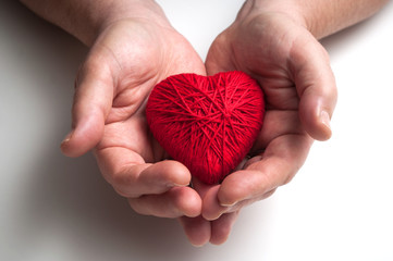 closeup of red wool heart in hand of woman on white table background