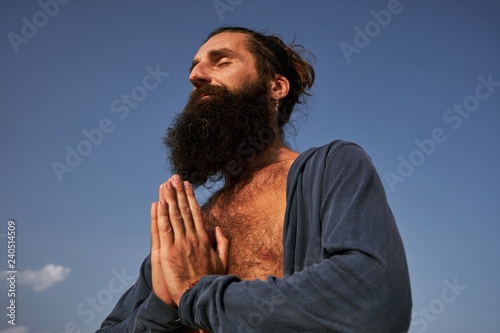 Fotografía handsome bearded male with namaste hands in blue clear sky background
