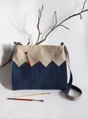 Crossbody bag is made of linen and decorated with knitted red decor. Light background