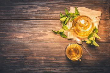  Fragrant fresh herbal tea of ​​mint and melissa in a glass cup and a teapot on a dark wooden background. Traditional herbal drink. Place for text or design. Flat layout. View from above. Toning