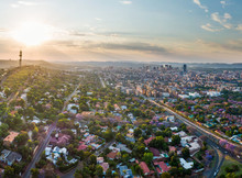 Aerial Panorama Of Pretoria City Skyline At Sunset. Jacaranda Trees In Suburb Of Muckleneuk Blooming. Telkom Tower, Sunnyside Apartment Buildings And Central Business District Behind. 