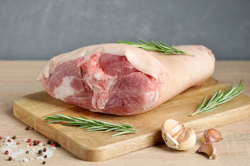 Wall Mural - Uncooked pork knuckle on a wooden tray. Rosemary, garlic, salt and pepper for pickling shank. Light gray background. Close-up.