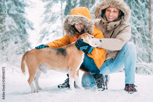 Fotomural Father and son; dressed in Warm Hooded Casual Parka Jacket Outerwear walking with their beagle dog; they petting him and smiling in snowy forest