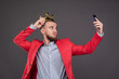 Young bearded handsome man in gold crown taking selfie looking at smartphone