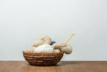 Close Up View Of Yarn With Knitting Needles In Wicker Basket On Wooden Tabletop On Grey Background