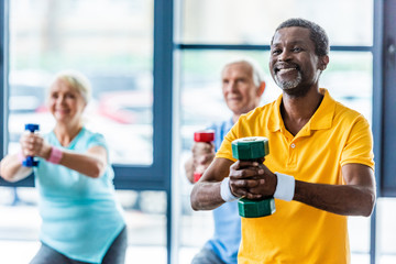 african american sportsman and his friends exercising with dumbbells at gym