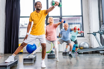 Wall Mural - senior sportspeople synchronous exercising with dumbbells on step platforms at gym