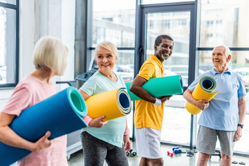 Wall Mural - happy multethnic senior athletes holding fitness mats at sports hall