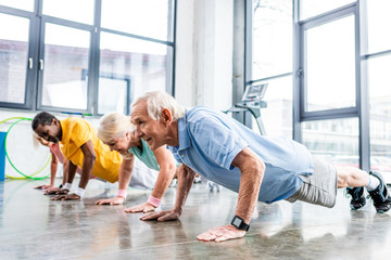 Wall Mural - cheerful multiethnic senior sportspeople synchronous doing plank at gym