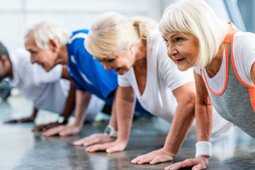 Wall Mural - selective focus of senior sportswoman and her friends doing plank at gym