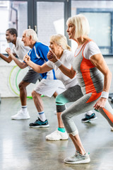 Wall Mural - side view of multiethnic senior sportspeople synchronous exercising at sports hall