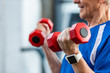 © LIGHTFIELD STUDIOS - partial view of of senior sportsman with smartwatch doing exercise with dumbbells at gym