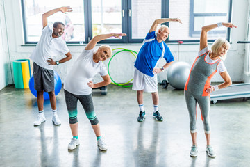 Wall Mural - high angle view of multiethnic senior sportspeople synchronous exercising at sports hall