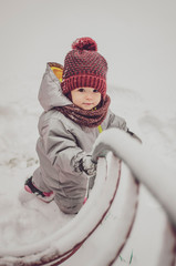 Canvas Print - Funny little child girl wearing in red hat, a scarf, and a warm winter suit with gloves having fun at winter day in beautiful winter park playing with snow