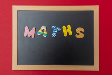Wall Mural - Black chalkboard with wooden frame, word, text maths in colorful letters, red wall background