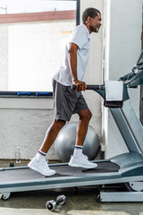 Wall Mural - side view of african american man running on treadmill at gym