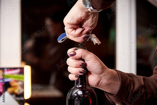 Fotografie, Obraz Girl opens a bottle of wine with a corkscrew close-up.