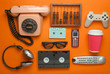Retro objects on orange background. Rotary telephone, audio cassette, video cassette, gamepad, 3d glasses, tv remote, headphones, push-button phone. Analog media technology of the past. Flat lay..