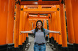 Young occidental woman doing sightseeing in the Fushimi Inari-taisha shrine in Japan. Walking the long way to the top full of red torii. Travel photography. Lifestyle.
