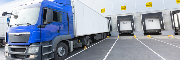 Loading dock of large warehouse with blue cabin truck under loading