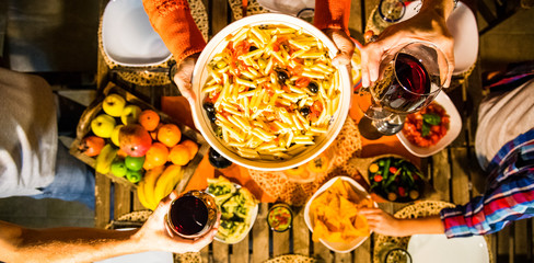 Group of friends two families eat together italian pasta and drink red wine - viewed from top and above - panoramic composition - colors and background with people celebrating and having fun together