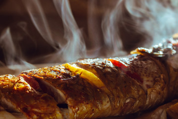 Fried tasty fish with lemon and tomato with smoke. Grilled fish with crisry crust and smoke above. Delicious cooked fish in sunlight. Baked seafood concept. Kitchen and cooking background. Fish meal.