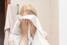 Woman drying and cleaning her face with a white towel