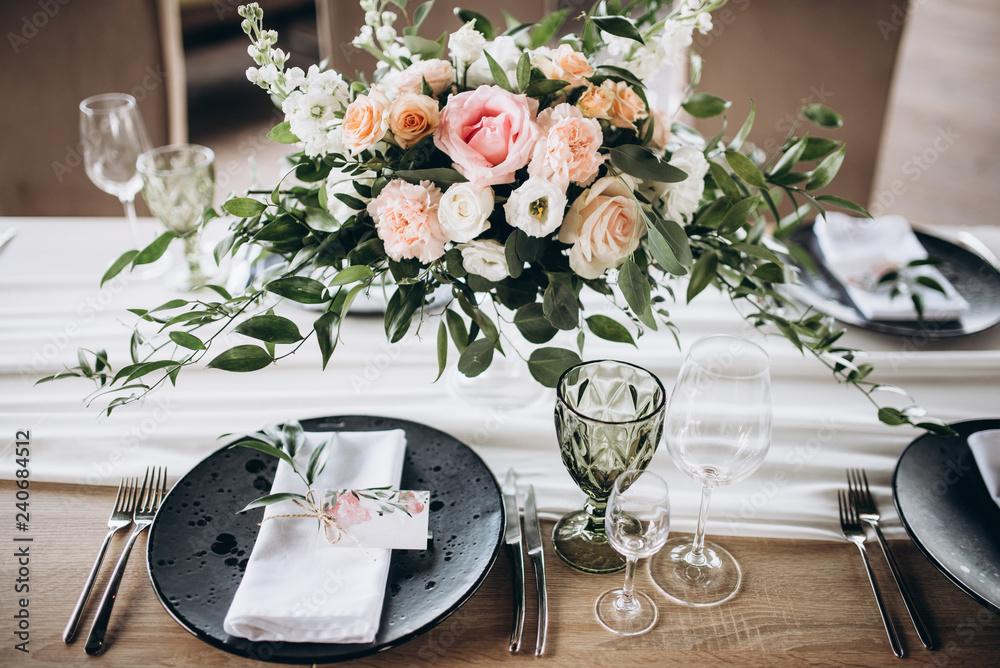 Wedding table serving. Wedding banquet. Beautiful festive table decorated with bouquet of flowers, black plate with card of name guest and cutlery. Top view - obrazy, fototapety, plakaty 