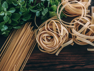 Uncooked dry pasta. Fettuccine and spaghetti with leaves of fresh basil. Italian food background.