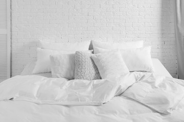 Canvas Print - Large comfortable bed with pillows and blanket near white brick wall indoors. Stylish interior