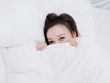 © atiger - Funny smiling Chinese girl covering half of face with white blanket, young happy woman hiding and peeking from duvet, feels sweet, wide awake, head shot close up, top view.