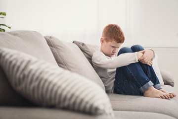 Offended boy sitting on sofa at home