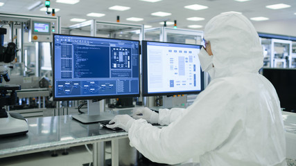 Wall Mural - Shot of a Scientists in Sterile Suits Working with Computers, Analyzing Data form Modern Industrial Machinery in the Laboratory. Product Manufacturing Process: Semiconductors, Biotechnology.