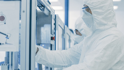 In the Manufacturing Facility Team of Scientist Wearing Sterile Protective Coverall Set's up / Programs Modern Industrial 3D Printer, High Precision Manufacture of Semiconductors under Process.